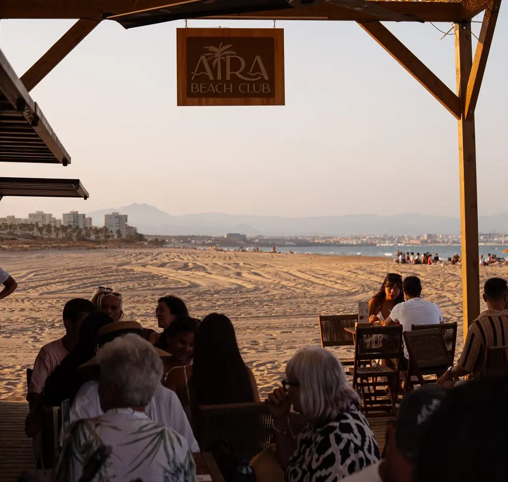 La terraza de Aira llena de gente al atardecer, con el cartel de madera del beach club